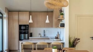 A modern kitchen with wooden cabinets, a central island, pendant lights, and a dining area with a wooden table and chairs. - Nordic Zen 2BR Beach House • Bali-Inspired Calm (Vārzas)