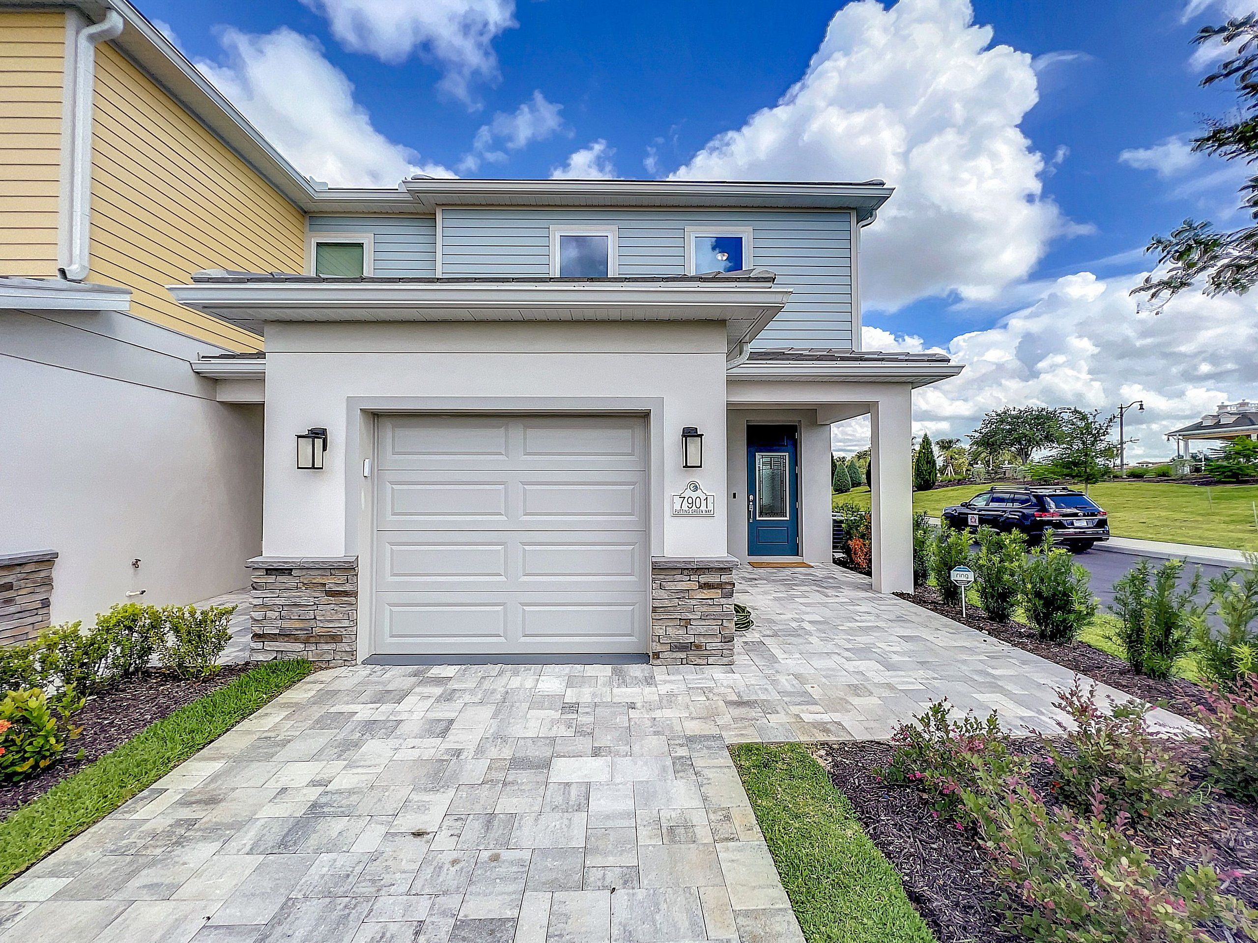 A modern two-story house with a white garage door, a blue front door, and a stone accent wall.