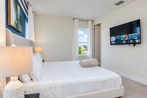 Habitación de hotel con cama, televisor montado en la pared, ventana con cortinas y lámpara de noche.