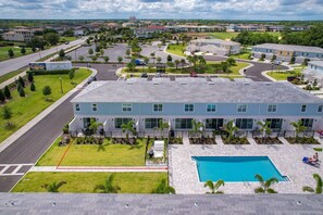 A modern building with a swimming pool, surrounded by a well-maintained lawn and palm trees. - Reunion 3BR Villa Near Disney + Pool Access (Kissimmee)
