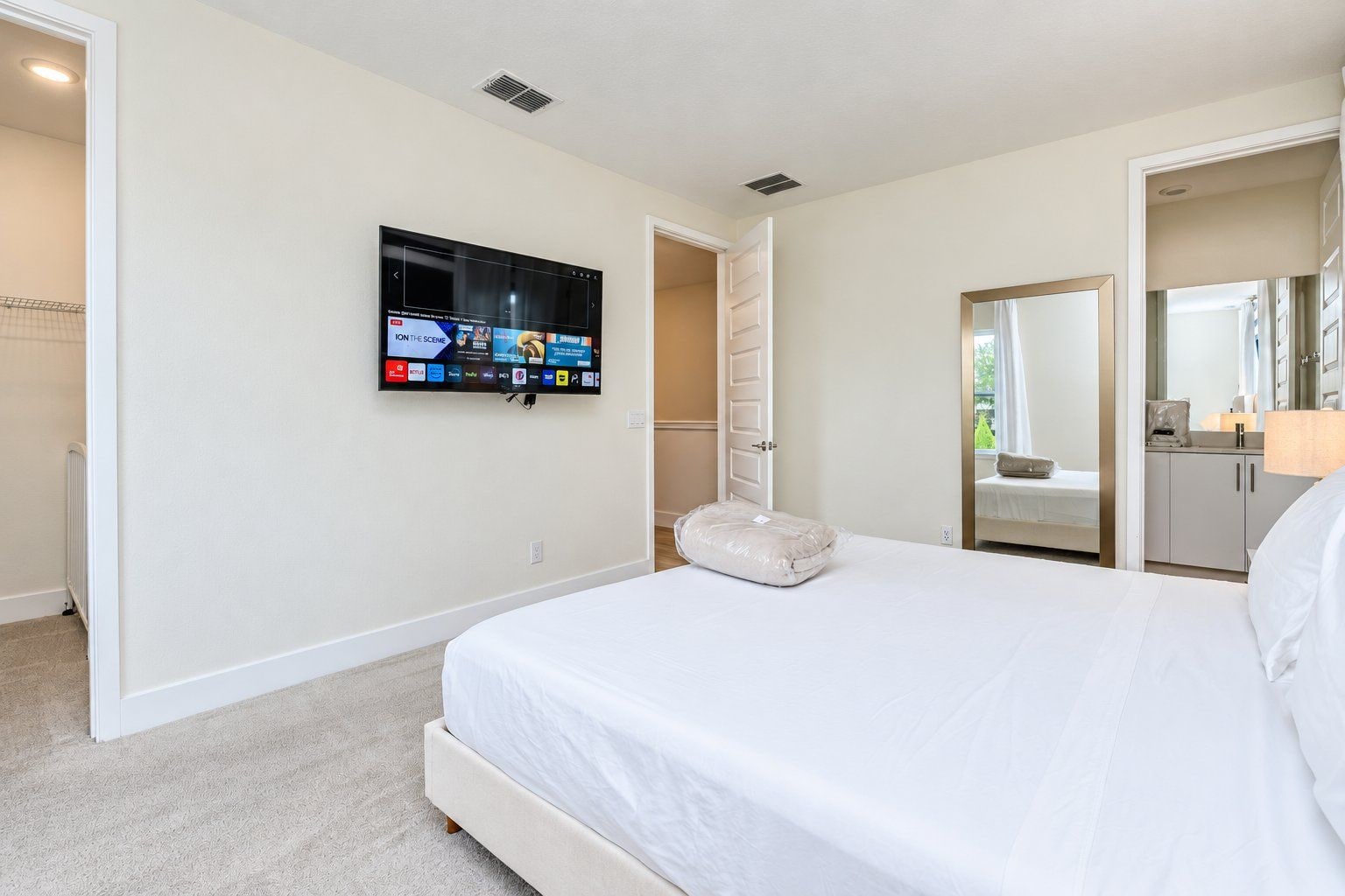 A hotel room with a large bed, a flat-screen TV mounted on the wall, a walk-in closet, and a bathroom visible through an open door.