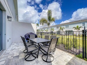 A patio with a table and chairs, a covered grill, and a view of a residential area with houses and palm trees. - Reunion 3BR Villa Near Disney + Pool Access (Kissimmee)