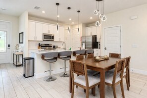 A modern kitchen with white cabinets, stainless steel appliances, and a central island with bar stools. - Reunion 3BR Villa Near Disney + Pool Access (Kissimmee)