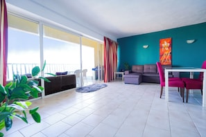 Una sala de estar moderna con balcón, comedor y una pared de acento color verde azulado.