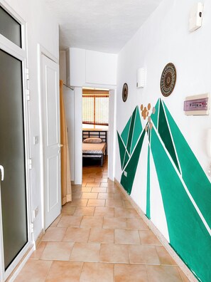 Un pasillo con una cama al fondo, una puerta a la izquierda y un muro con diseños geométricos.