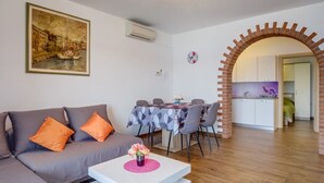 Sala de estar com sofá, mesa de jantar e cozinha visíveis por um arco.