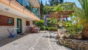 En innergård med ett stengolv, utemöbler, en pergola med klätterväxter och en stenmur.