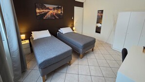 A hotel room with two single beds, a desk, a wardrobe, and a cityscape painting on the wall. - RHO FIERA FLAT- 100 M FROM THE METRO (Pero)