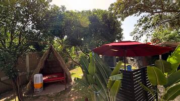 A thatched-roof hut with a fan, a red umbrella, and lush greenery.