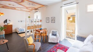 Un soggiorno luminoso con zona pranzo, un divano, un tappeto decorato e un soffitto con motivo ornamentale.