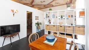 Un soggiorno moderno con un tavolo da pranzo in legno, un televisore a schermo piatto e una scaffalatura bianca con cesti e oggetti decorativi.