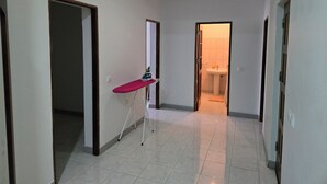 Un couloir avec un sol carrelé, une porte donnant sur une salle de bain et une planche à repasser au milieu.