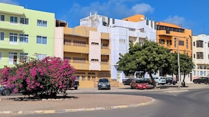 Une vue de rue avec des bâtiments aux couleurs vives, un arbre et des voitures garées.