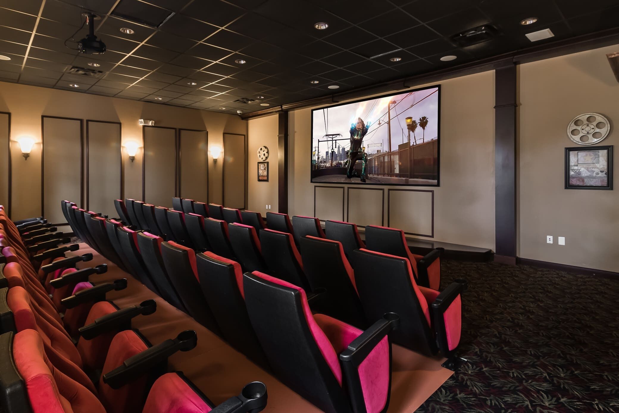 Ein Theater mit Reihen aus roten und schwarzen Sitzen, einer großen Leinwand und Wandleuchten.