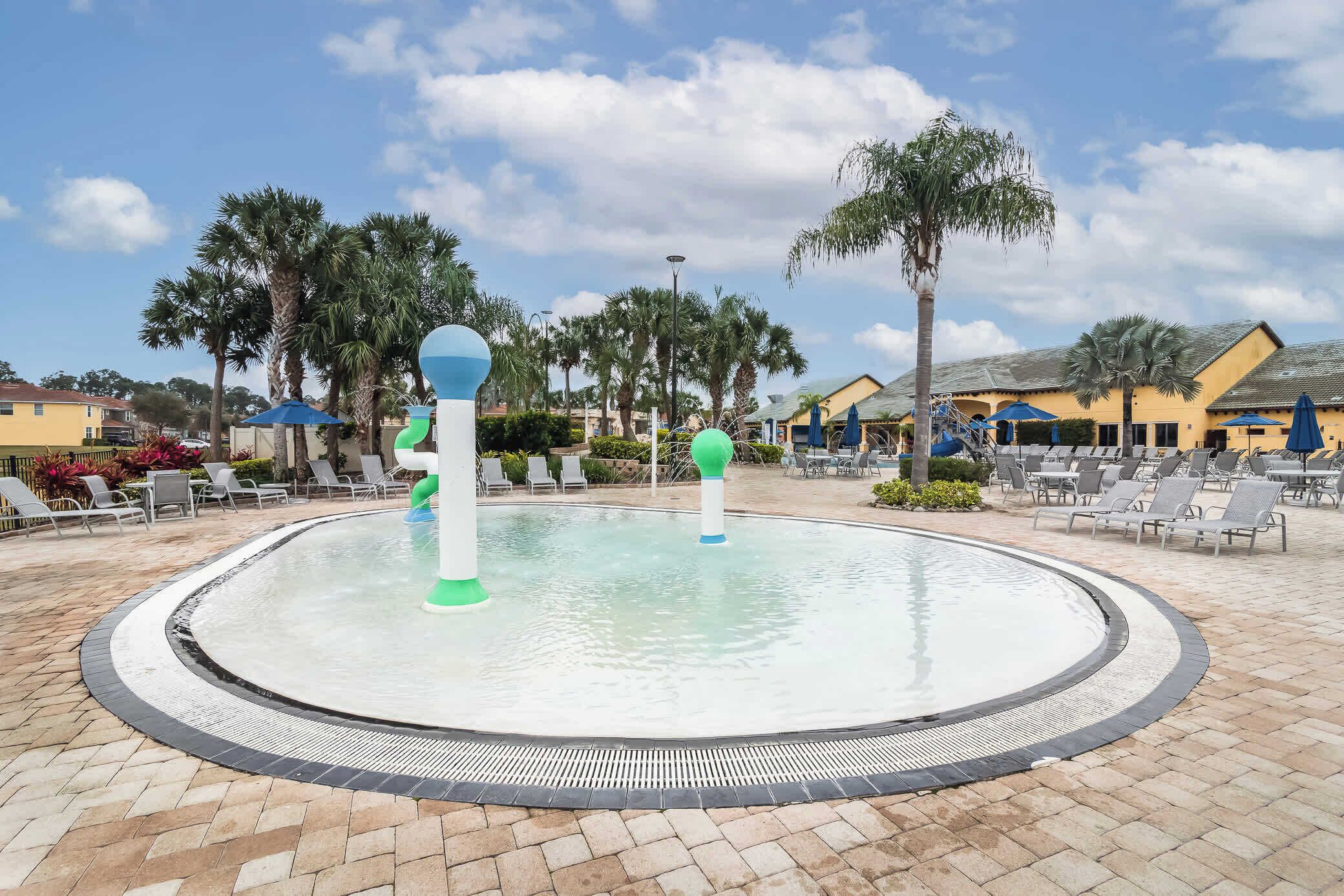 A circular pool with a water fountain, surrounded by lounge chairs and palm trees.
