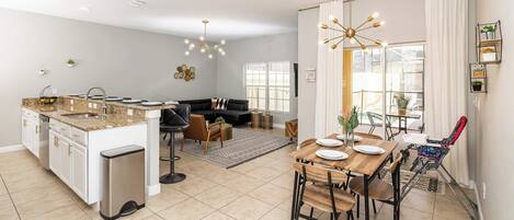 A modern kitchen with a dining area, a sofa, and a view of the outdoors.
