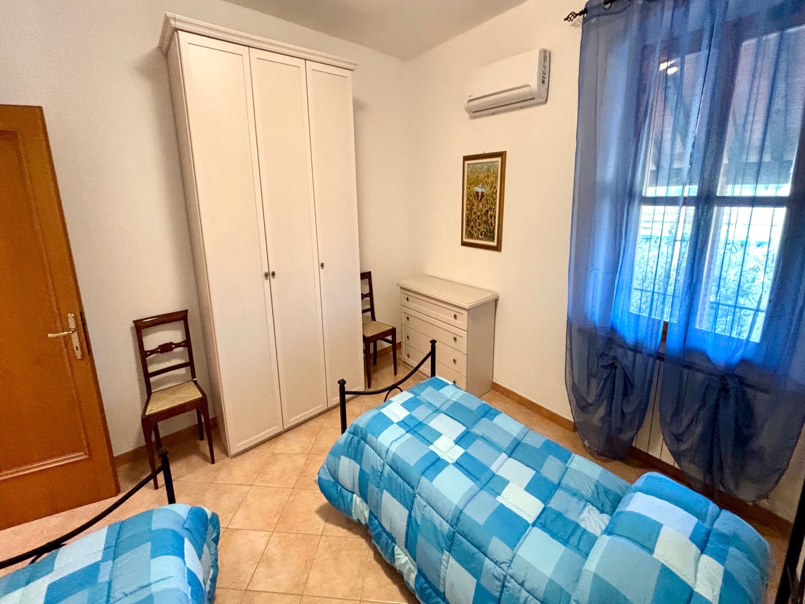 A bedroom with two beds, a wardrobe, a desk, and a chair.