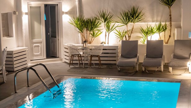 Una piscina con una zona de estar hundida, rodeada de sillas de descanso y plantas en macetas.