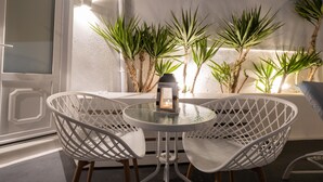 Una mesa redonda de vidrio con sillas de alambre blancas, un farol y plantas en macetas frente a una pared blanca.