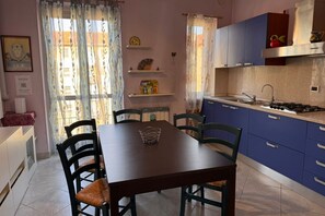 A dining area with a table and chairs, a kitchen with blue cabinets, and a window with curtains. - GuestHost - A comfortable and welcoming 70 square meters apartment, perfect for four people, located on the third floor of a building (NO elevator).The property is located in a quiet area and well-connected to the city center, reachable in about 20 minut (Alessandria)
