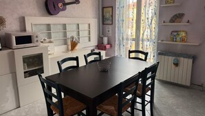Een eetgedeelte met een tafel, stoelen, een magnetron, een gitaar en decoratieve items op planken.