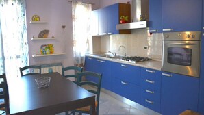 Een keuken met blauwe kastjes, een gasfornuis, een oven en een eettafel met stoelen.