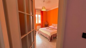 Een slaapkamer met een bed, een raam met gordijnen, een radiator en een hanglamp.