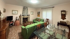 A living room with a fireplace, green sofa, dining table, and a clock on the wall.