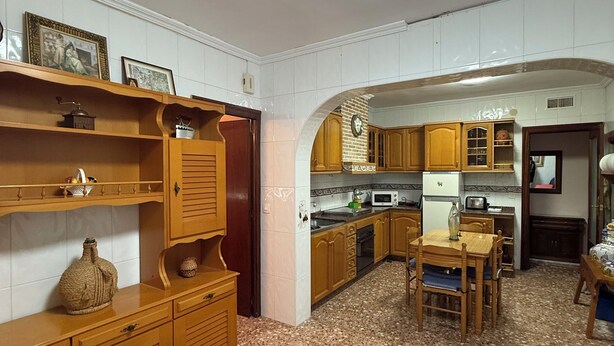 A kitchen with wooden cabinets, a dining table, and a tiled floor.