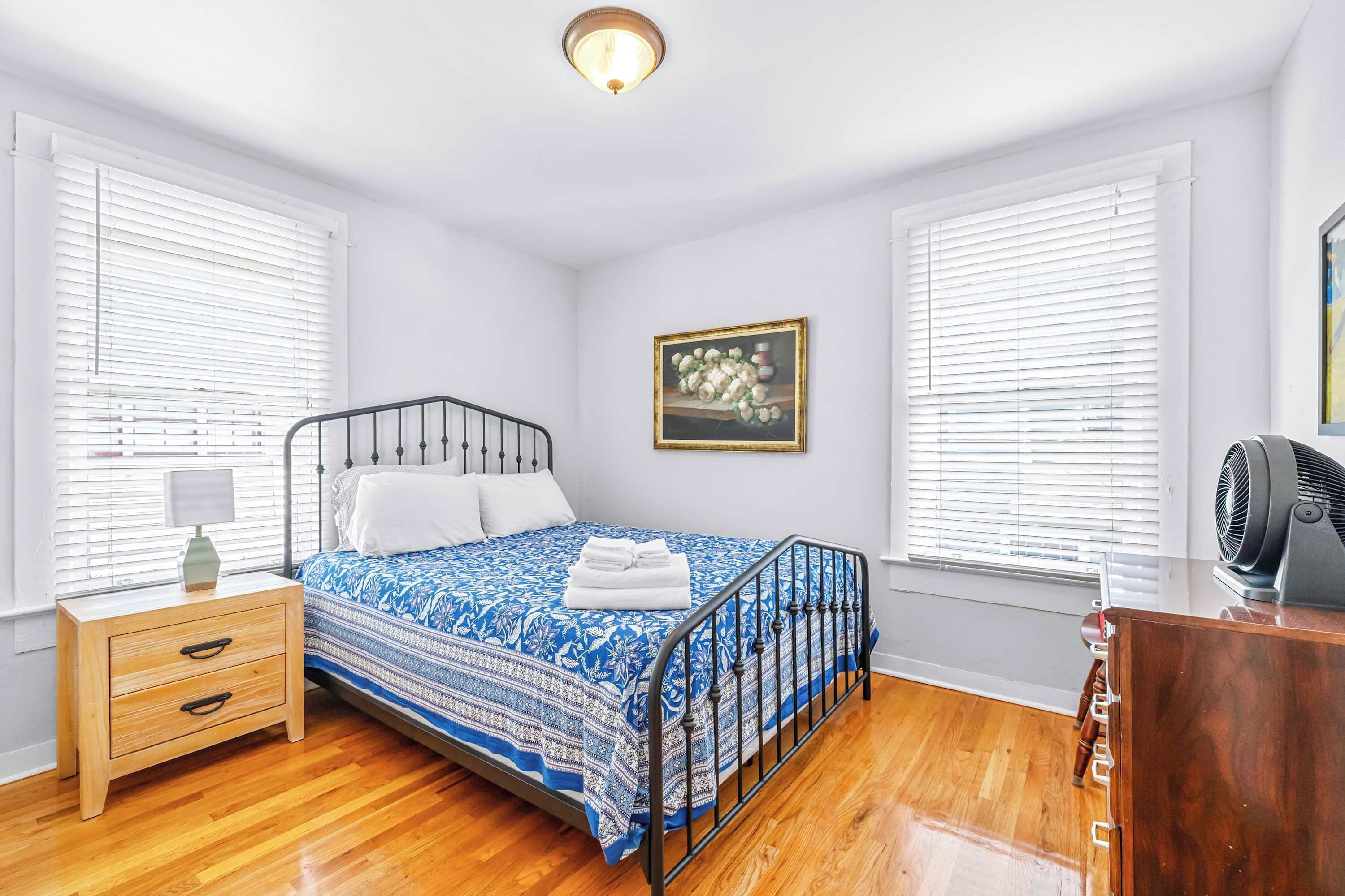 A bedroom with a bed, bedside table, lamp, and a fan.