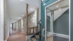 Un pasillo con paredes de piedra, barandilla de madera y puerta de ascensor de cristal.