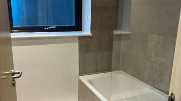 A bathroom with a bathtub, a window, and tiled walls.