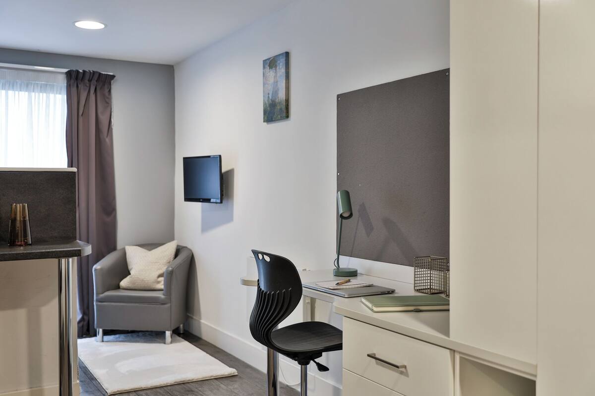 A modern bedroom with a desk, chair, and a television on the wall.