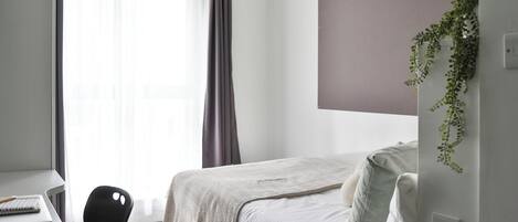 A minimalist hotel room with a bed, a desk, and a chair.