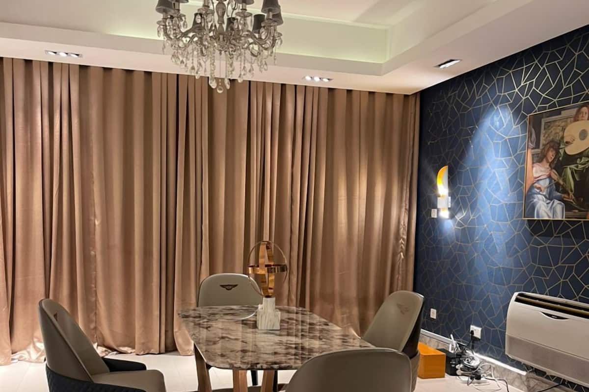 A dining area with a chandelier, a table, chairs, and a patterned rug.
