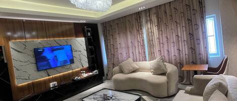 A modern living room with a large flat-screen TV, a chandelier, and a patterned wall.