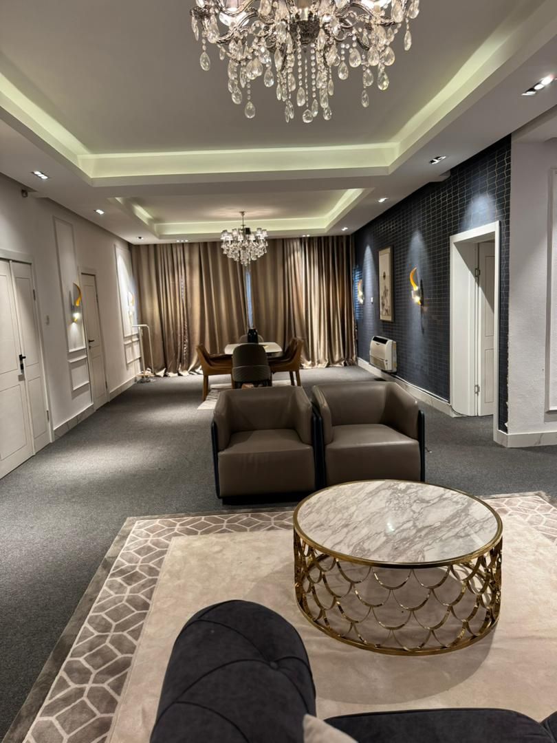 A spacious living area with a chandelier, leather sofas, a marble coffee table, and a dining table set for four.