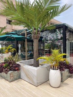 A palm tree in a planter, outdoor seating area, and a glass building with floral decorations. - Sujimoto Residences Precious  (Lagos)