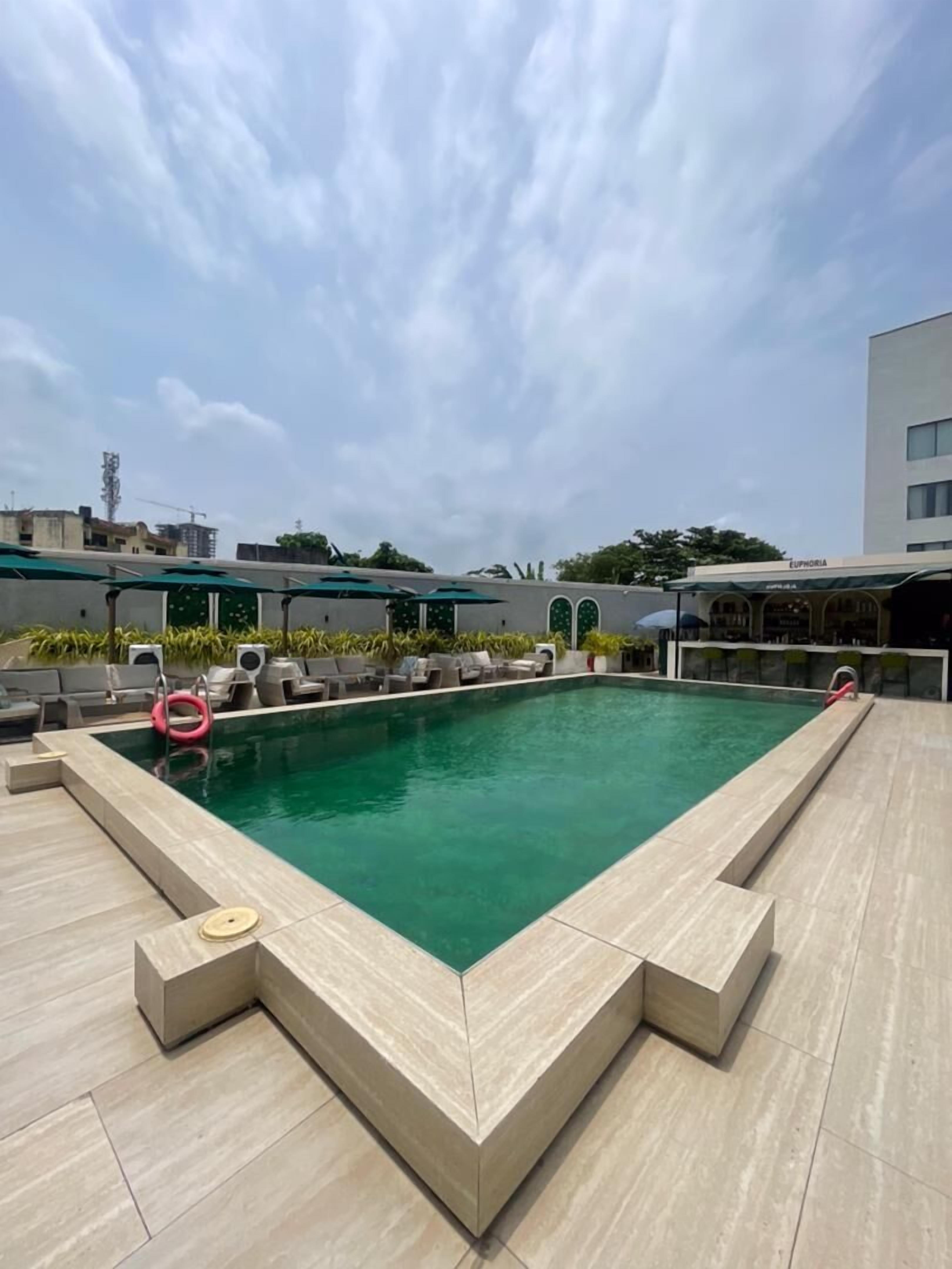 A rooftop pool with lounge chairs and umbrellas, surrounded by buildings.