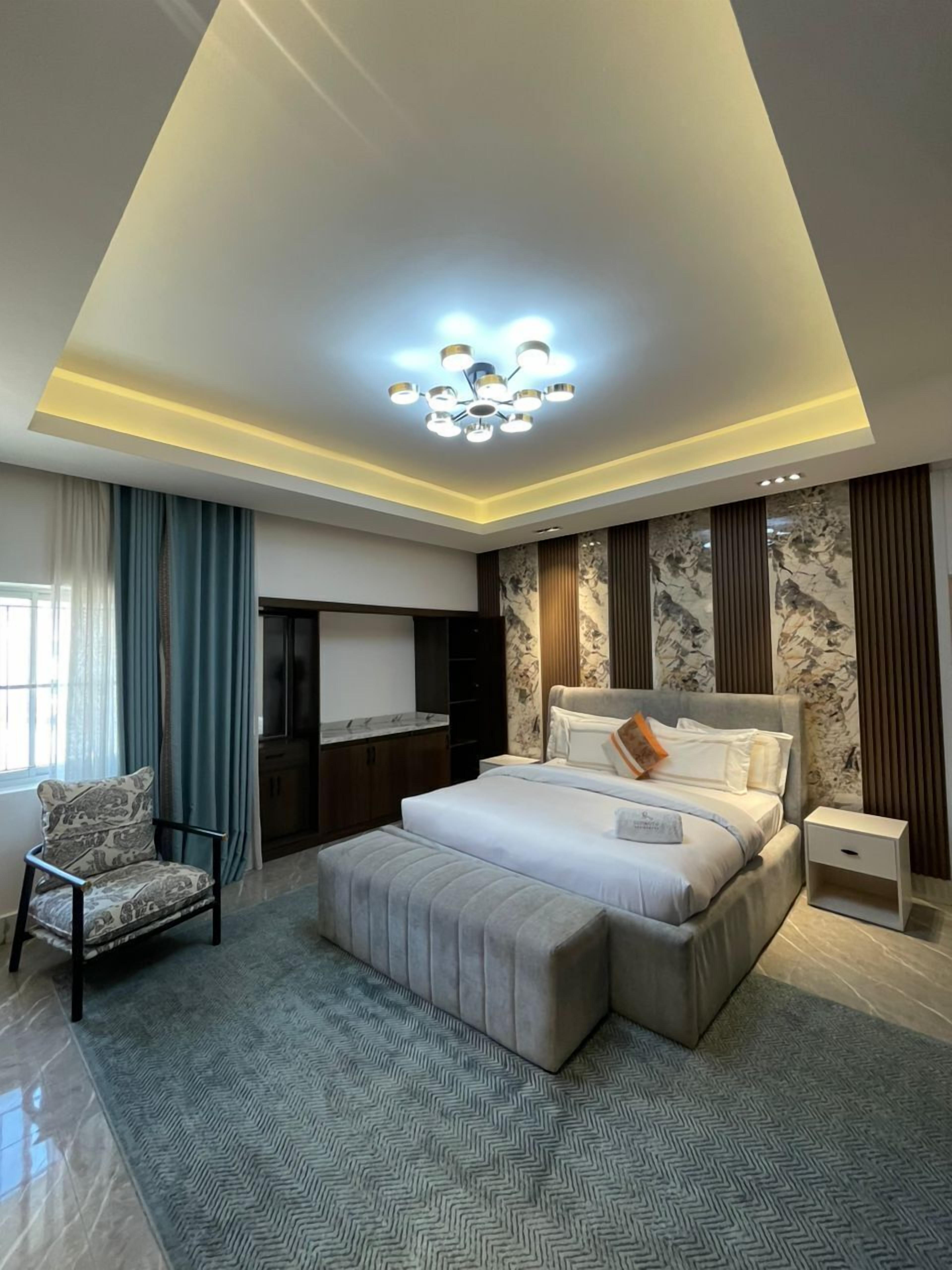 A modern bedroom with a large bed, a seating area, a TV, and a ceiling light fixture.