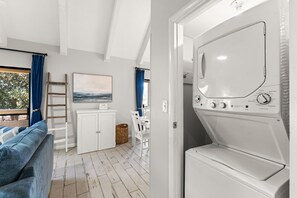 A laundry room with a front-loading washing machine, a wooden ladder, a white cabinet, and a painting on the wall. - Seascape Resort 34C | Beach Access | 5 Pools (Miramar Beach)