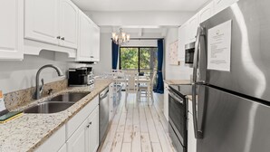 Una cocina moderna con armarios blancos, electrodomésticos de acero inoxidable, encimeras de granito y vistas al exterior.
