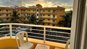 A balcony with two plastic chairs and a small table, overlooking a swimming pool and a building complex with multiple balconies. - Villa Sol Appartements Punta Canada (Punta Cana)
