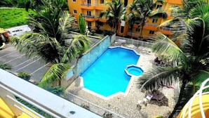 A pool surrounded by palm trees and a yellow building with balconies. - Villa Sol Appartements Punta Canada (Punta Cana)
