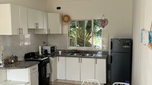 A compact kitchen with white cabinets, a black refrigerator, and a dining area with a table and chairs. - Villa Sol Appartements Punta Canada (Punta Cana)
