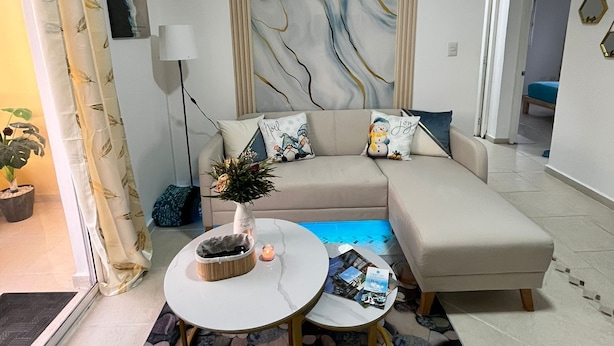 A modern living room with a beige sofa, a coffee table, and a decorative wall. - Villa Sol Appartements Punta Canada (Punta Cana)