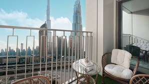 Un balcon avec une table en verre et des chaises en osier, donnant sur un paysage urbain avec de hauts immeubles et une autoroute.