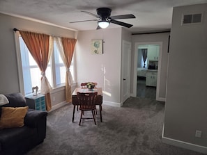 A living room with a dark-colored sofa, a dining table with chairs, a ceiling fan, and a window with curtains. - Charming 1-bedroom building with AC in Springfield (Springfield)