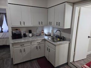 A compact kitchen with white cabinets, a granite countertop, a sink, and a coffee maker. - Charming 1-bedroom building with AC in Springfield (Springfield)