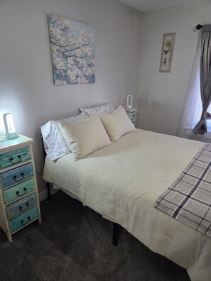 A bedroom with a bed, a nightstand with a lamp, a dresser, and a painting on the wall. - Charming 1-bedroom building with AC in Springfield (Springfield)